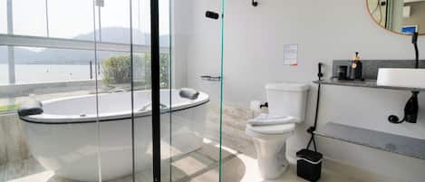 Een moderne badkamer met een glazen jacuzzi, toilet en een wastafel met aanrechtblad.
