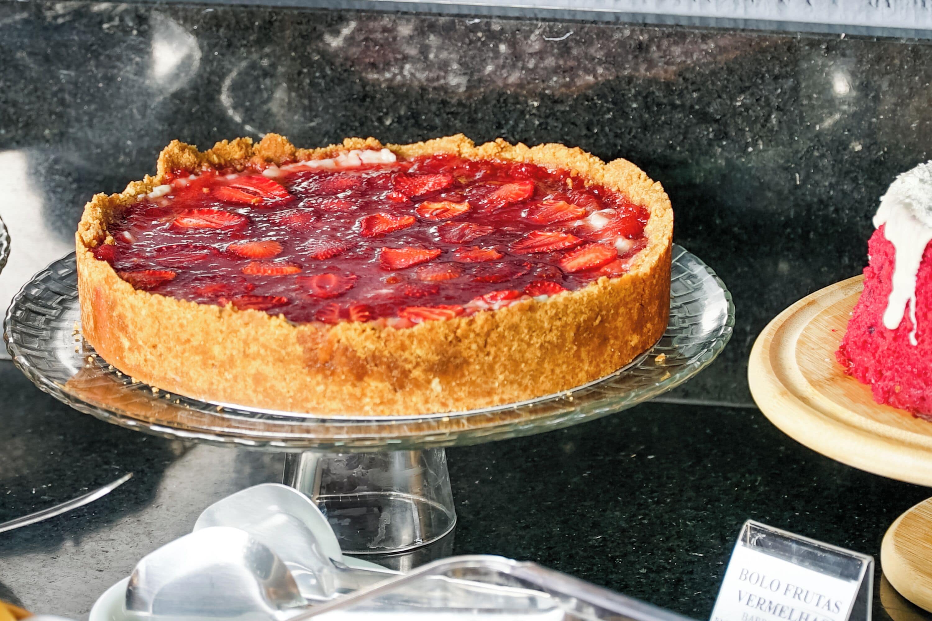 A dessert display with a strawberry tart on a glass stand.