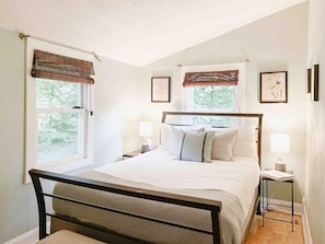 A bedroom with a bed, two bedside tables, two lamps, and a window with a view of trees. - Chic Treehouse Cabin with Pedal Boat, Hot Tub, BBQ, Fire Pit, SUPs, & Lake Access (Smallwood)
