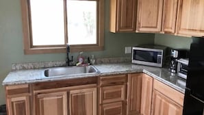 Una cucina con mobili in legno, un lavandino in acciaio inossidabile, un forno a microonde e un frigorifero.