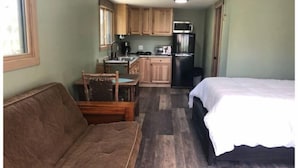 Una stanza compatta con un letto, un divano, un tavolo da pranzo con sedie, angolo cottura con microonde, frigorifero e ventilatore a soffitto.