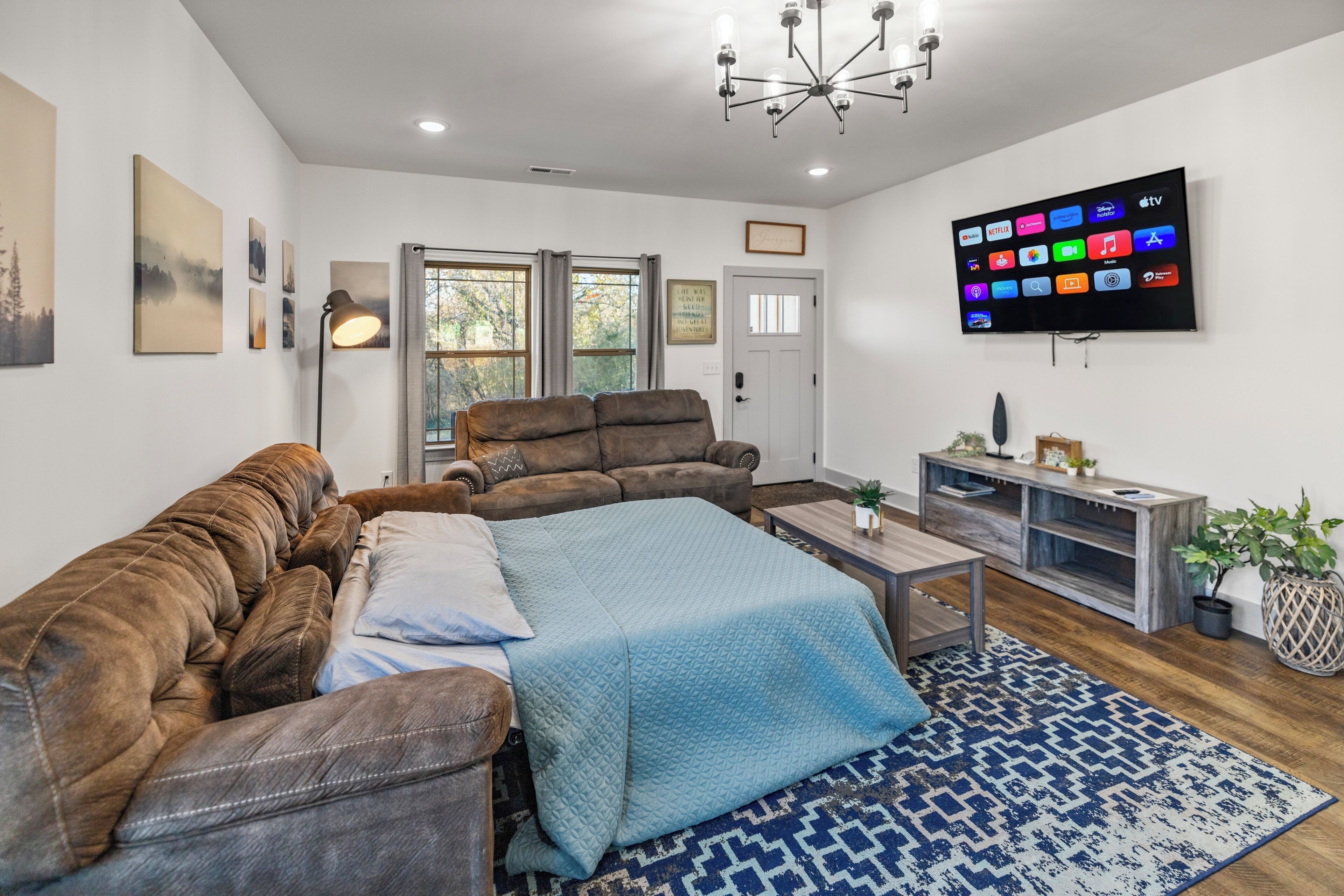 Ett modernt vardagsrum med en brun lädersoffa, ett blått, quiltat överkast, ett soffbord i trä och en stor, platt-TV som är monterad på väggen.