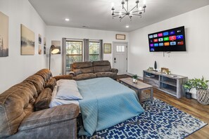 Una sala moderna con un sofá de cuero marrón, una colcha azul acolchada, una mesa de centro de madera y un televisor de pantalla plana grande montado en la pared.