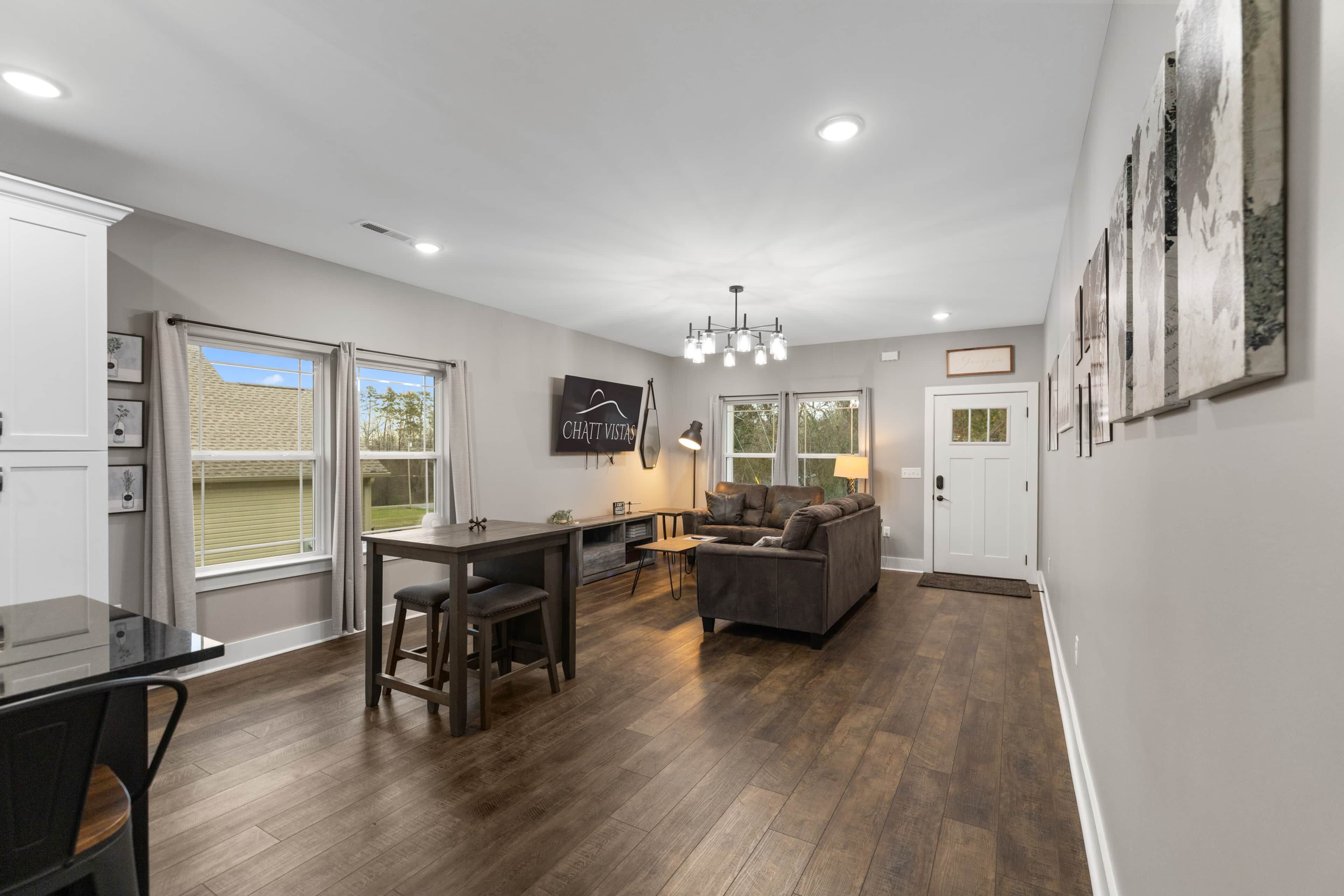 A spacious living area with a dining table, sofa, and a TV mounted on the wall.
