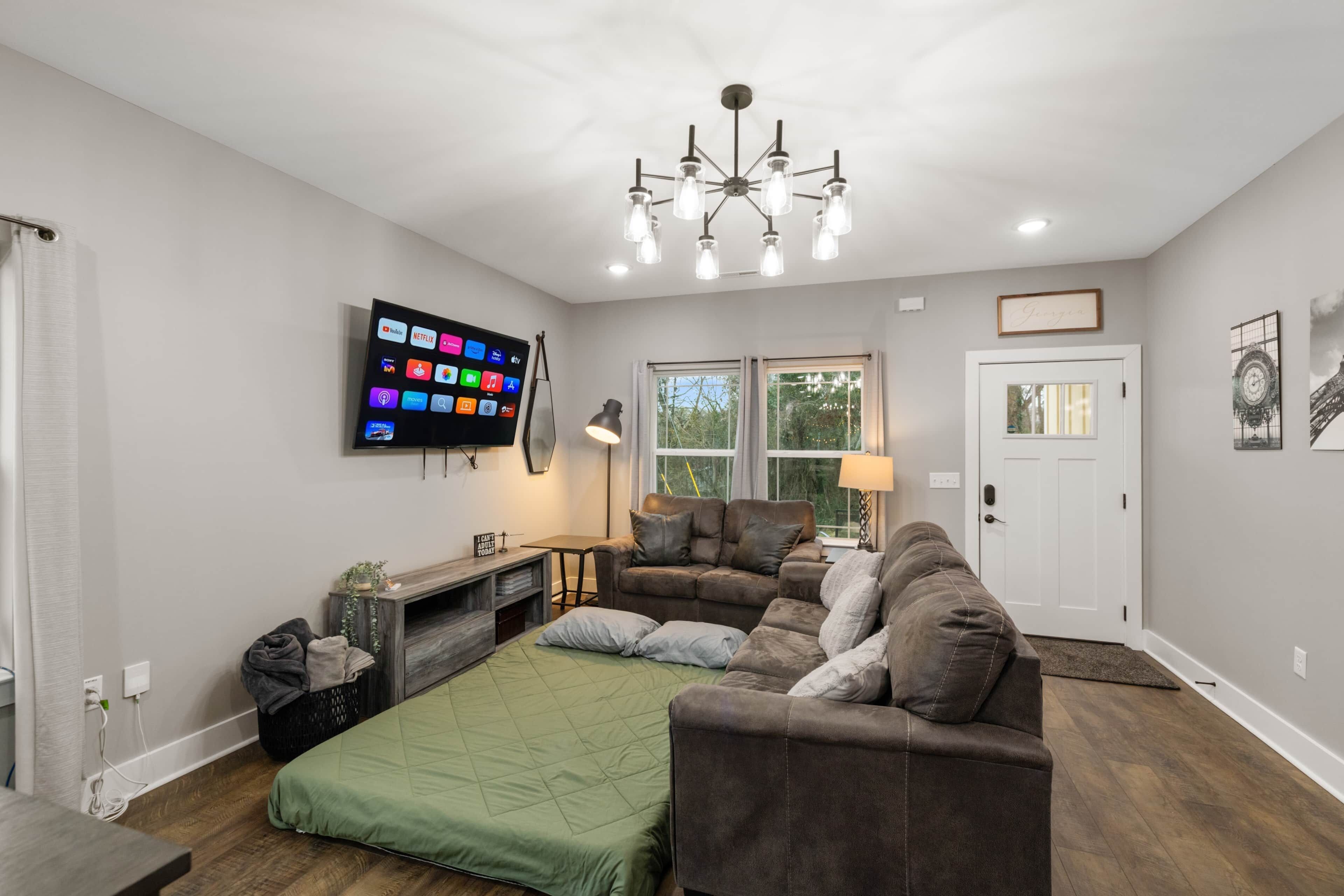 A living room with a flat-screen TV, a chandelier, a sofa, a coffee table, and a fireplace.