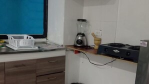 Una pequeña cocina americana con una licuadora, un cubo de basura y una ventana con cortinas azules.