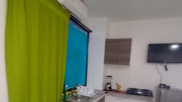 Cocina compacta con lavamanos, un pequeño comedor con dos sillas, un televisor montado en la pared y un cubo de basura.