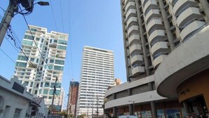 Vista de calle con un edificio alto con balcones, un edificio más pequeño de fachada curva, y una calle con vehículos y peatones.