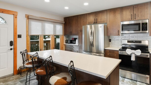 A modern kitchen with stainless steel appliances, a large island with bar stools, and wooden cabinets.