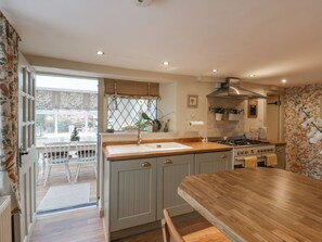A kitchen with a wooden countertop, a stove, and a sink. There is a window with a view of the outside. - Laurel Cottage (Guisborough)