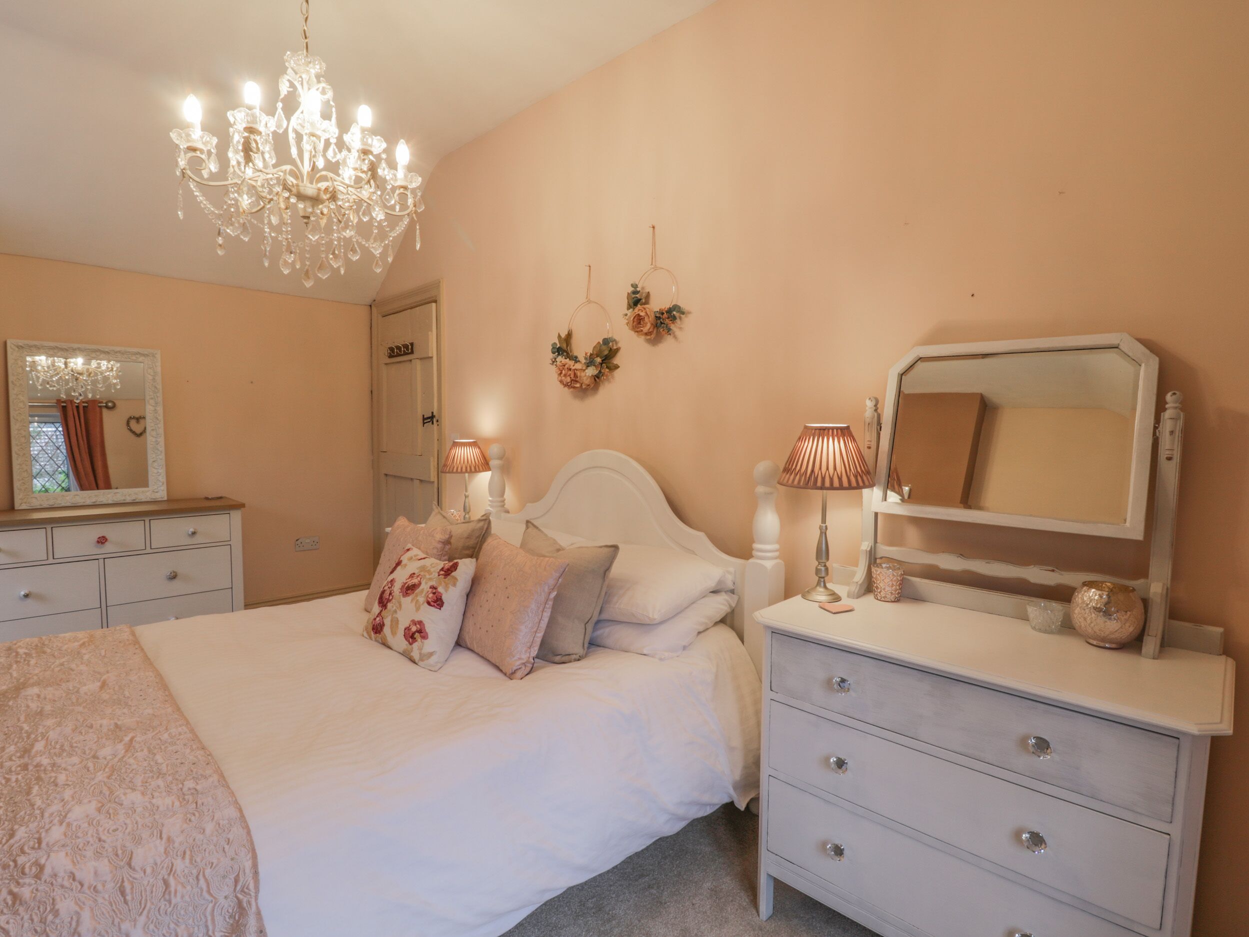 A bedroom with a bed, dresser, mirror, chandelier, and wall decorations.