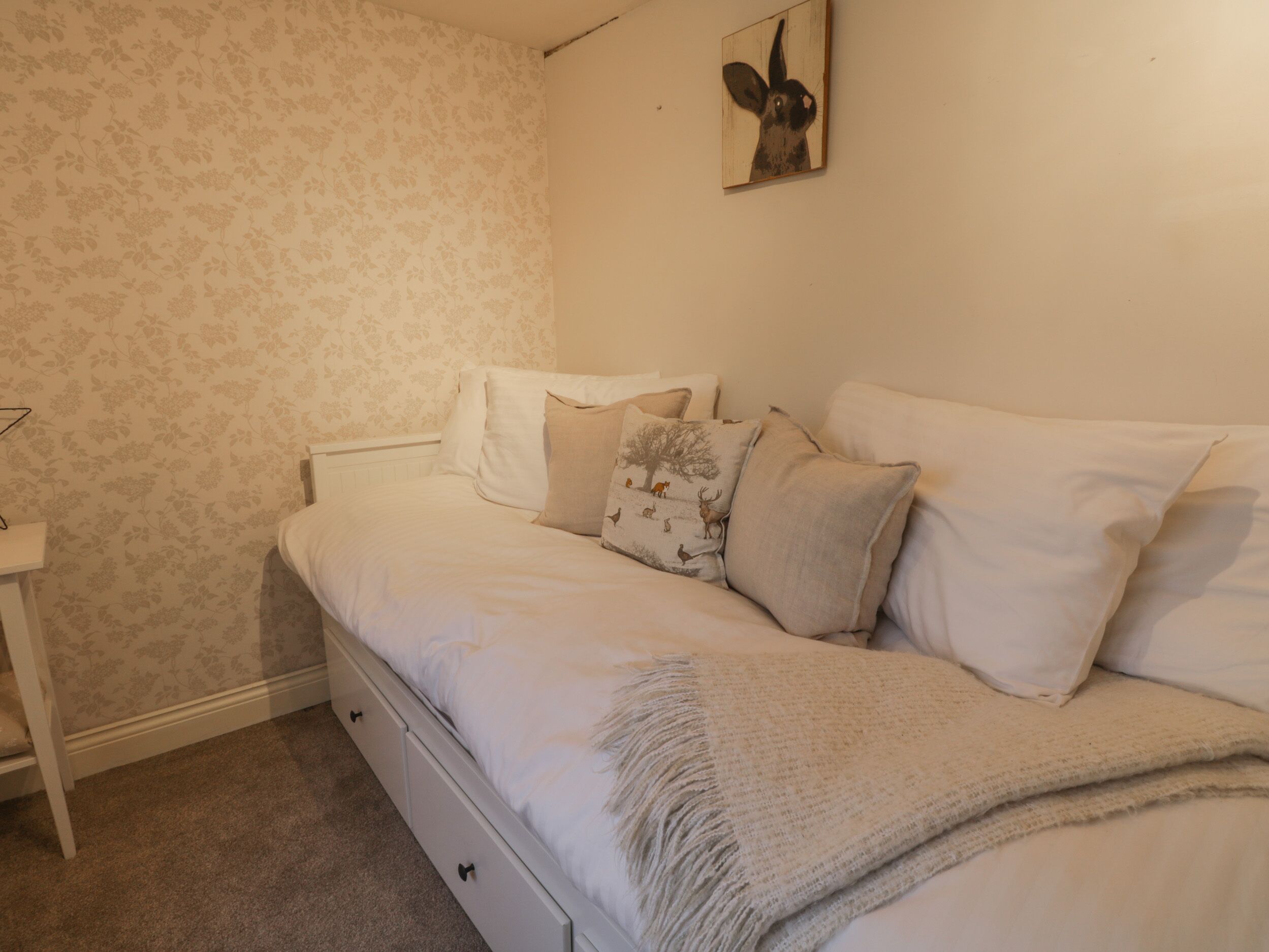 A bedroom with a bed, pillows, a nightstand, and a wall-mounted picture.