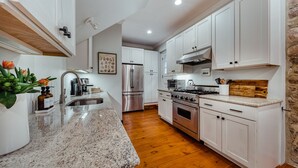 Una cocina moderna con armarios blancos, electrodomésticos de acero inoxidable, encimera de granito y suelo de madera.