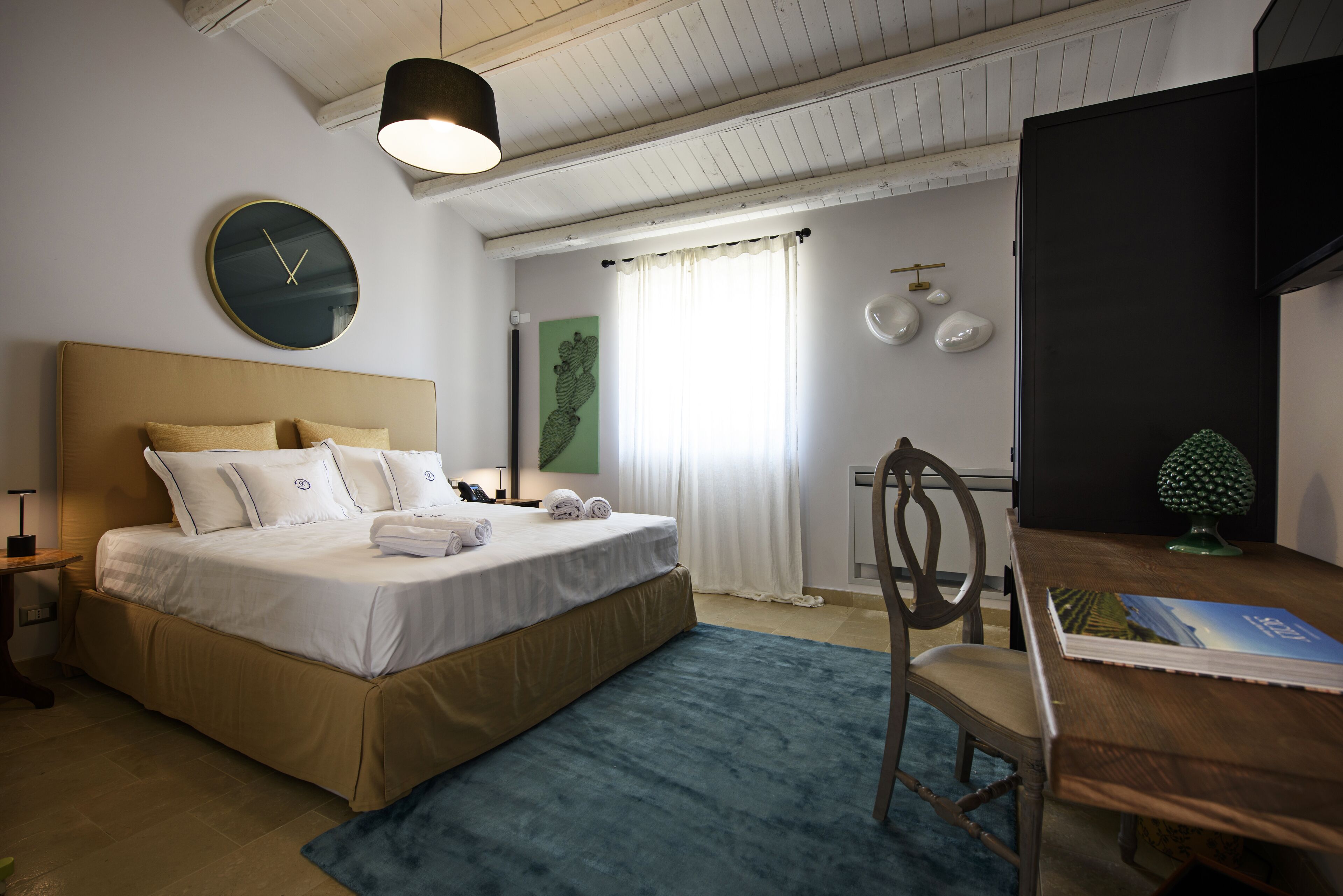 A bedroom with a bed, a desk, a chair, a clock, and a window with curtains.