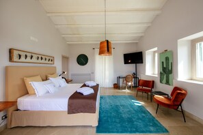 Quarto de hotel moderno com uma cama grande, uma escrivaninha, uma cadeira, televisão e obras de arte nas paredes.