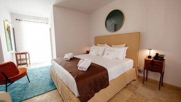A hotel room with a bed, a chair, a bedside table with a lamp, and a clock on the wall.