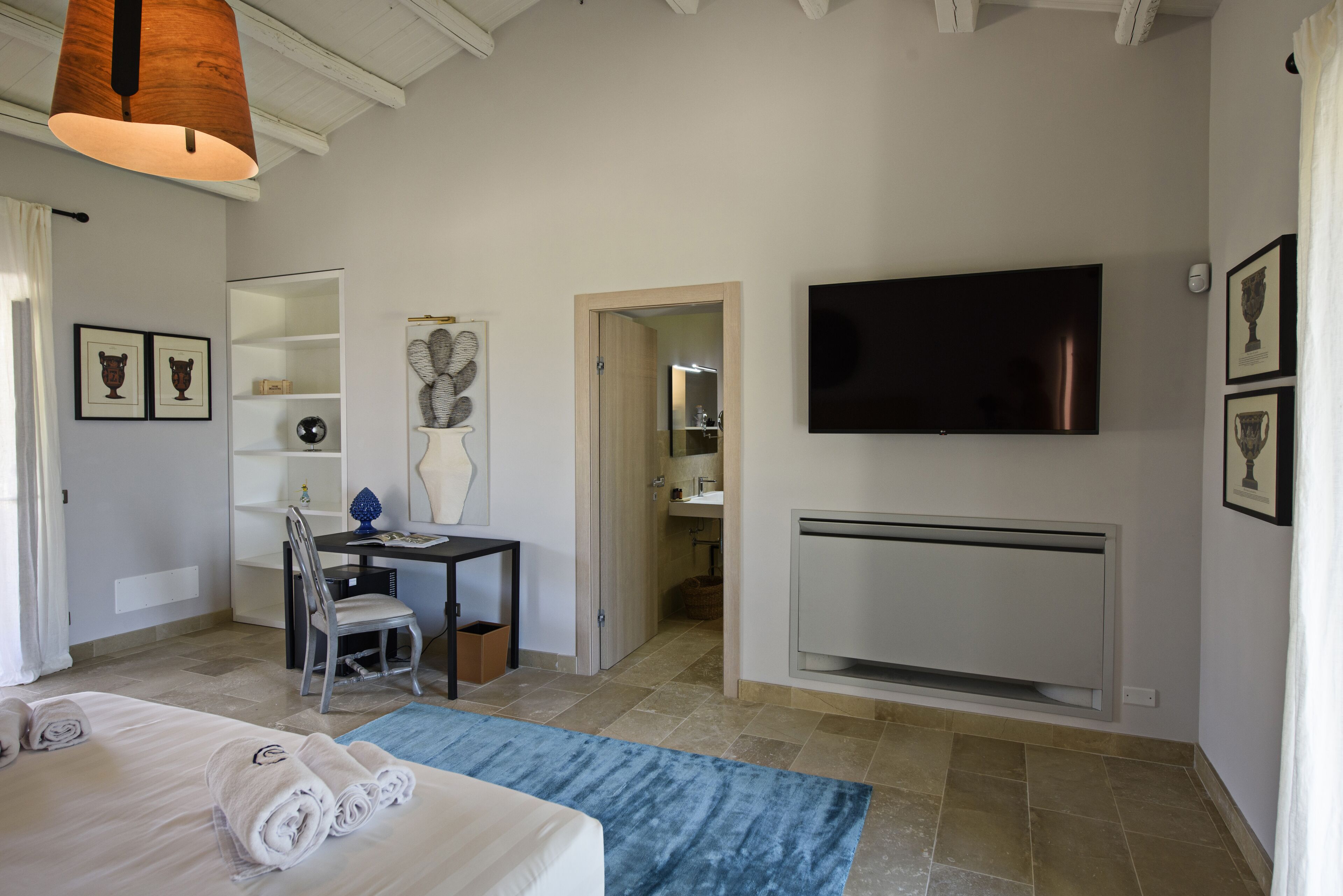 A hotel room with a bed, a desk, a chair, a television, and a bathroom visible through an open door.