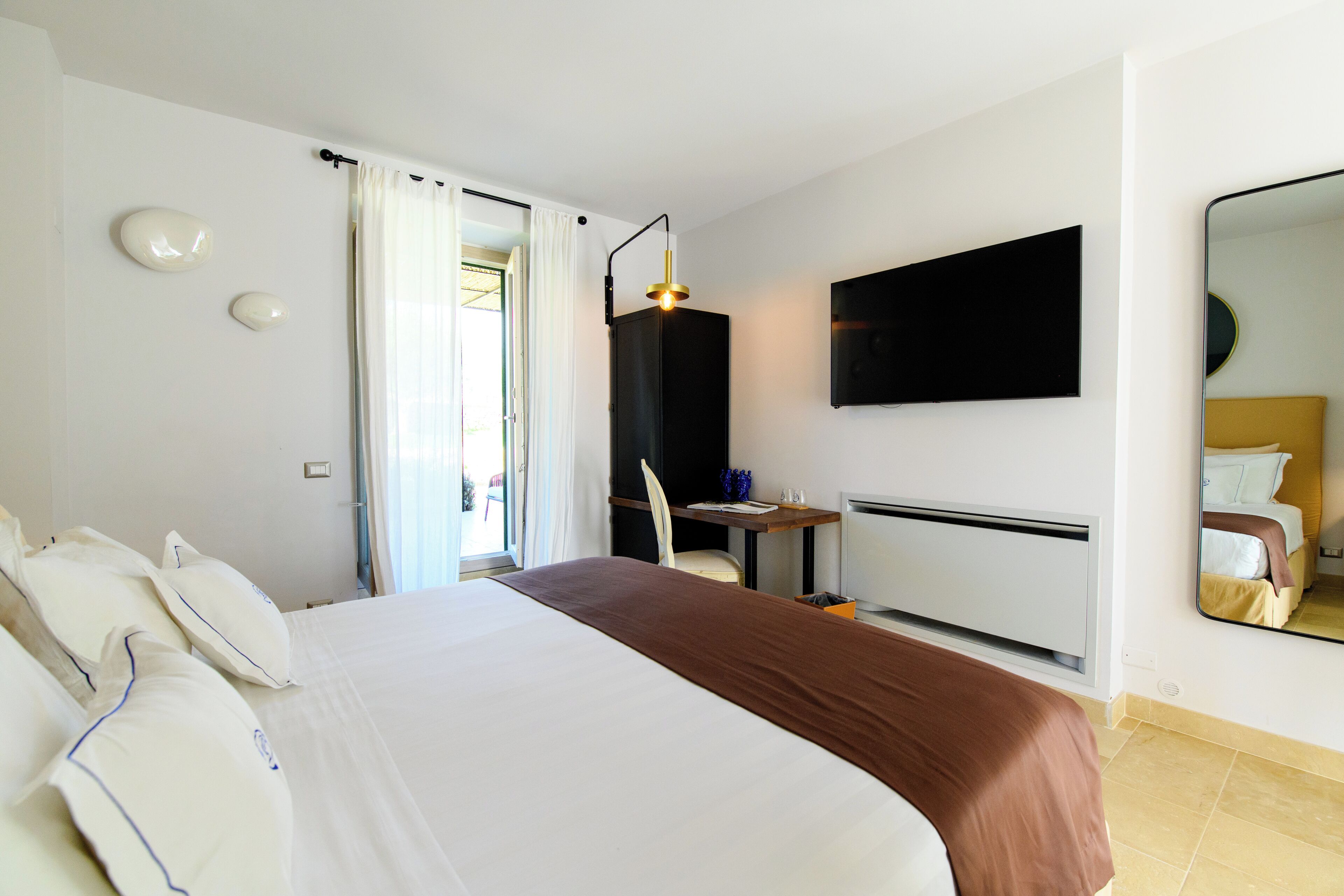 Ein Hotelzimmer mit Bett, Schreibtisch, Stuhl, einem an der Wand befestigten Fernseher und einem Spiegel.