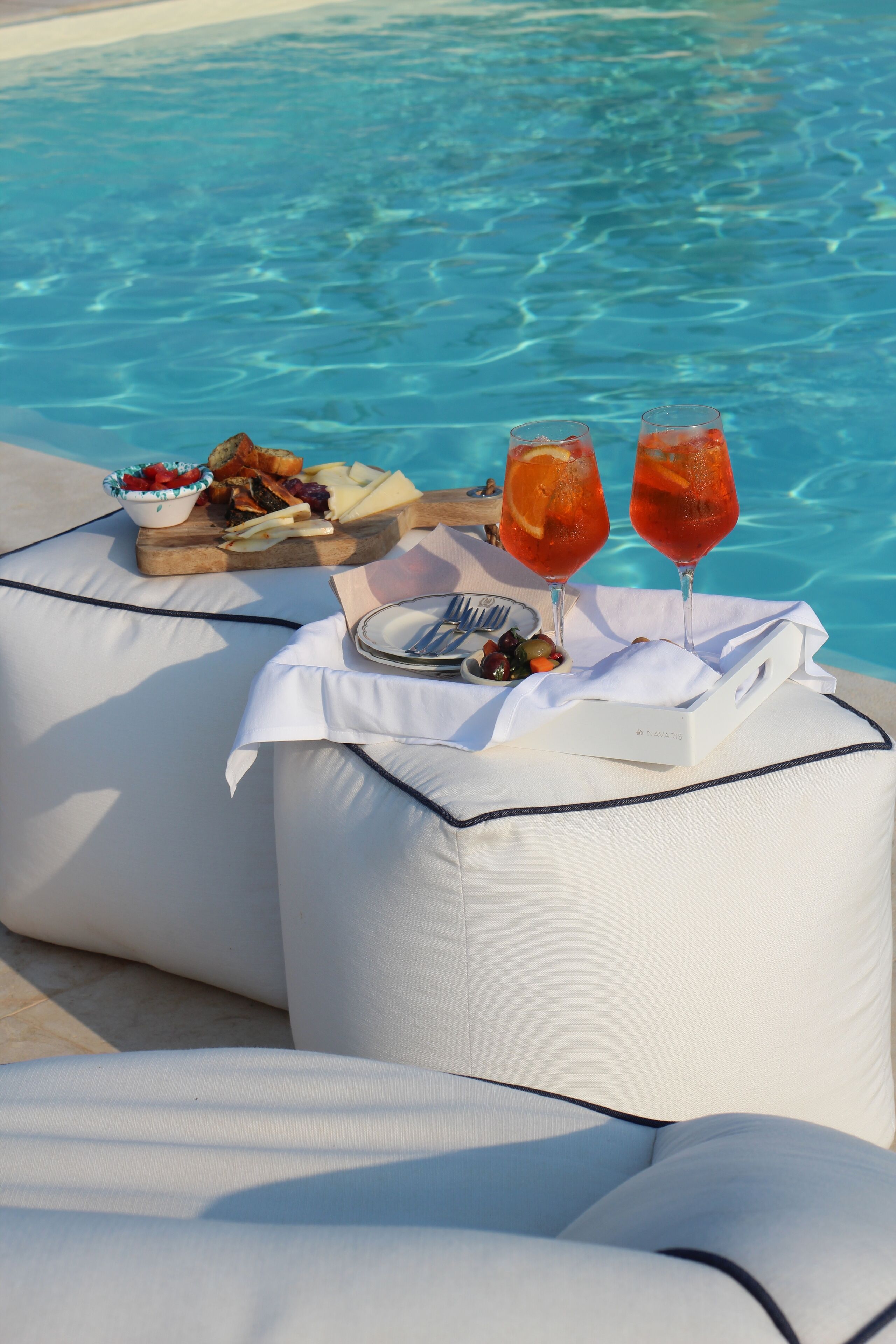 Tavolo, cuscini, cibo e bevande disposti a bordo piscina.