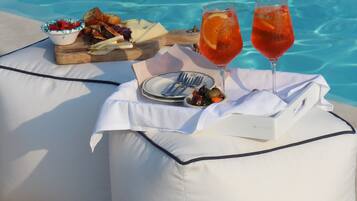 Tavolo, cuscini, cibo e bevande disposti a bordo piscina.