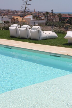 A swimming pool with clear water, surrounded by a grassy area with white lounge chairs. - POGGIO LEANO  (Scicli)