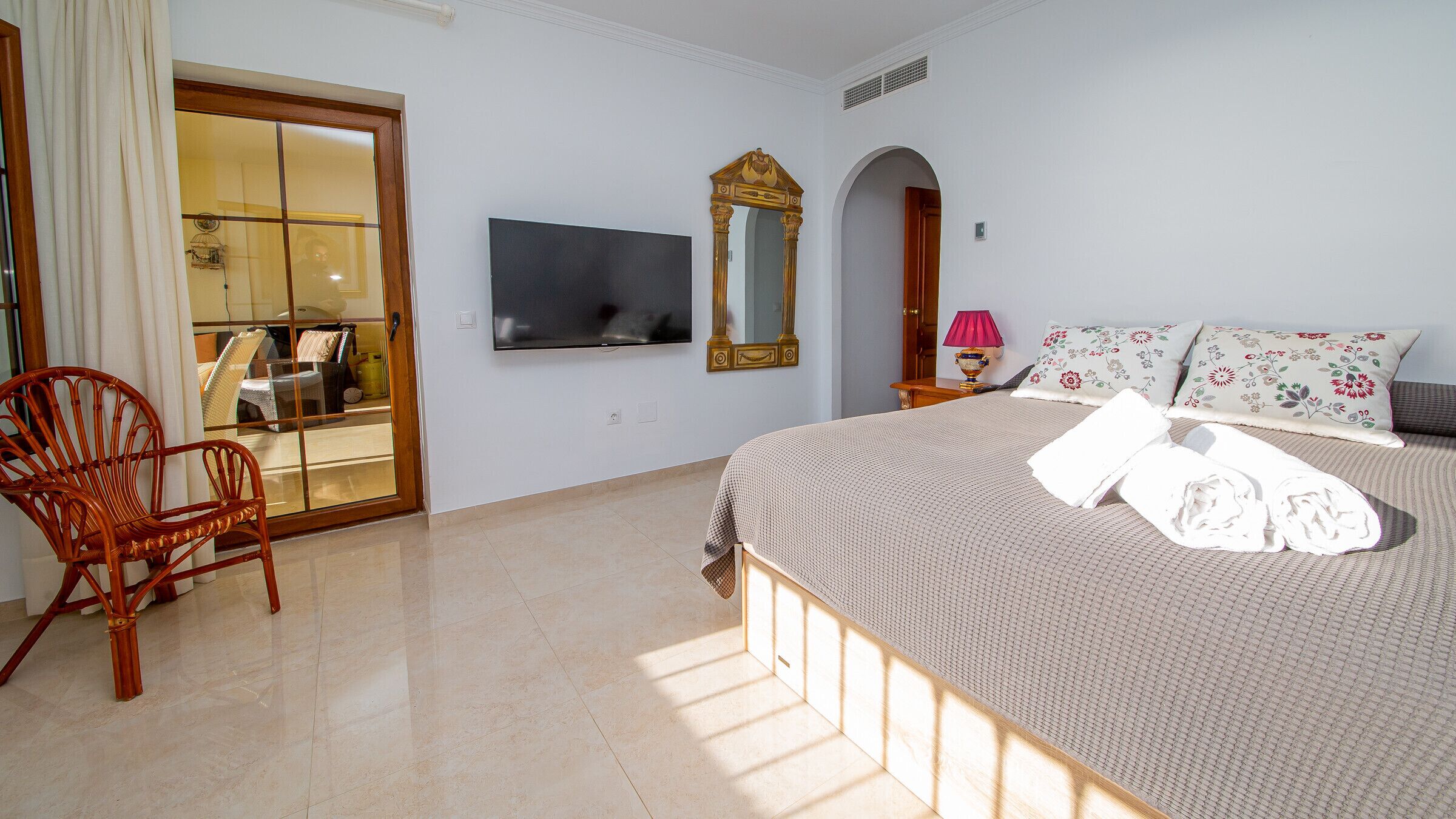 Ein Hotelzimmer mit Bett, Fernseher, Spiegel, Stuhl und einer Tür zum Balkon.