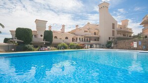 Ein Swimmingpool mit Liegestühlen und Sonnenschirmen, umgeben von einem großen Gebäude mit mehreren Balkonen und einem Turm.