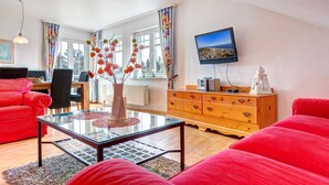 Ein Wohnzimmer mit einem roten Sofa, einem Glastisch, einer Holzkommode und einem Fernseher an der Wand.
