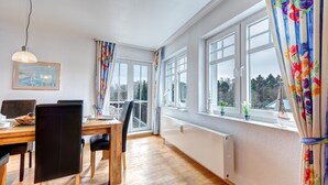 Ein Essbereich mit Holztisch, schwarzen Stühlen, einer hängenden Leuchte und großen Fenstern mit Vorhängen.