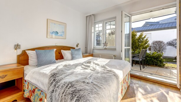 Ein Schlafzimmer mit einem großen Bett, einem Holznachttisch, einem Fenster mit Blick ins Freie und einem Bild an der Wand.