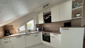 Eine moderne Küche mit weißen Schränken, einer Mikrowelle, einer Kaffeemaschine und einem Fenster mit Jalousien.