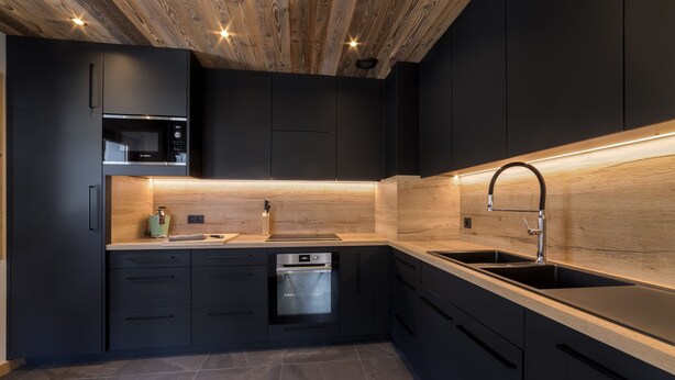 A modern kitchen with dark cabinetry, a wooden ceiling, and built-in appliances. - Fully renovated La Datcha family chalet, ski room and playroom (Les Contamines-Montjoie)