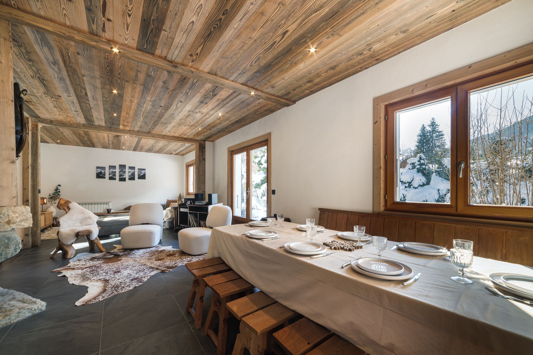 Un espace repas avec une longue table dressée pour quatre personnes, des bancs en bois et un plafond rustique.