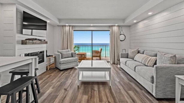 A modern living room with a large window, a dining area, and a kitchen.