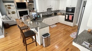A modern kitchen with white cabinets, granite countertops, and a central island with bar stools. - 2025 Masters Golf Tournament Rental (Evans)