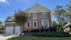 A two-story brick house with a front garage, a well-maintained lawn, and a small tree in the front yard. - 2025 Masters Golf Tournament Rental (Evans)