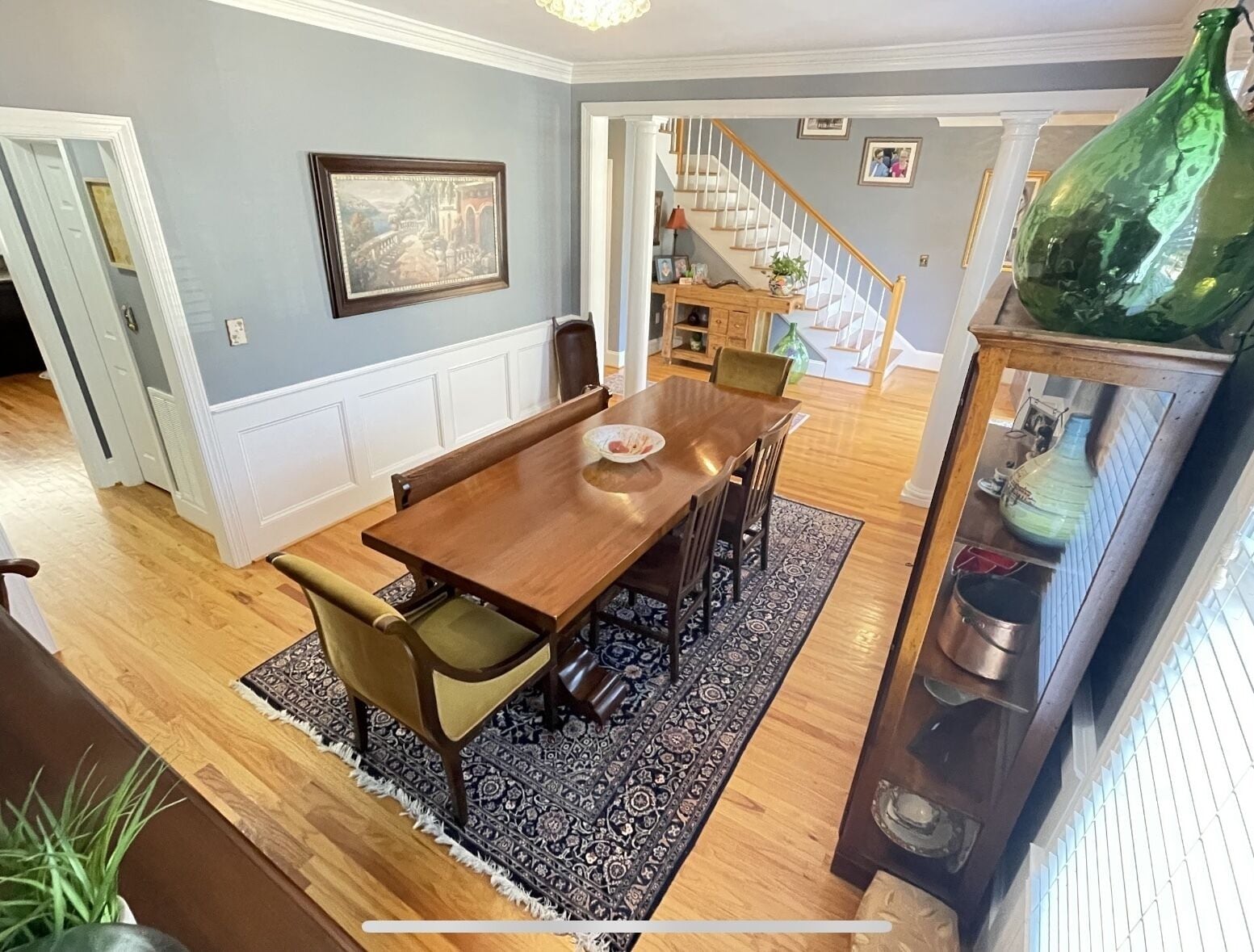 A dining area with a wooden table and chairs, a patterned rug, and a green vase on a cabinet.