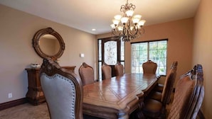 A dining room with a large wooden table and leather chairs, a chandelier, and a large mirror on the wall.