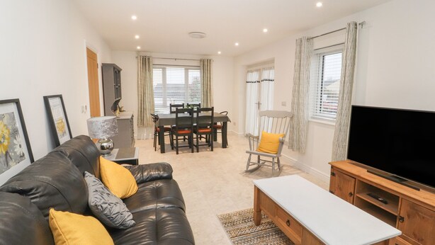A modern living room with a leather sofa, a wooden TV stand, and a dining area with a table and chairs.