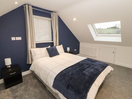 A bedroom with a bed, a nightstand, a window with curtains, a skylight, and a radiator.