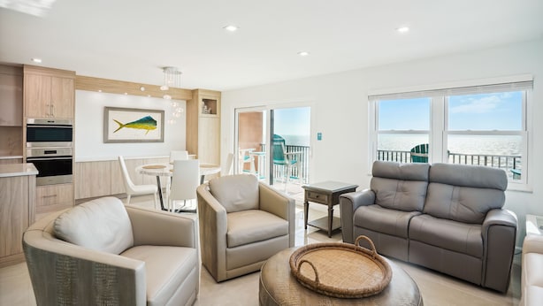 Ein modernes Wohnzimmer mit einer Couch, Sesseln und einem Essbereich. Ein großes Fenster bietet Blick auf das Meer.
