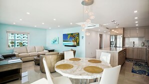 Ein modernes Wohnzimmer mit einem runden Esstisch, beigen Sofas und einer Küche mit Holzschränken und Edelstahlgeräten.