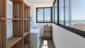 En lille balkon med havudsigt, en vaskemaskine og træhylder.