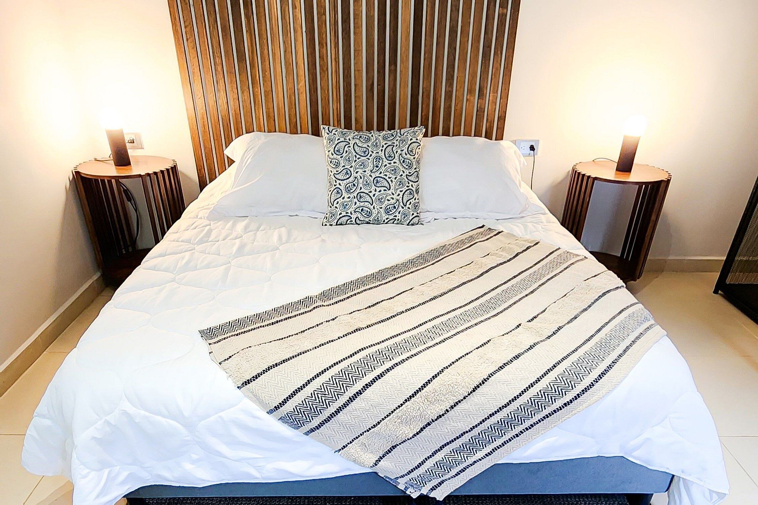 A neatly made bed with a patterned blanket, two bedside tables with lamps, and a wooden headboard.