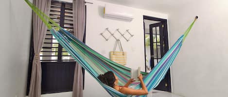 Una habitación con una hamaca, una ventana con cortinas, un aire acondicionado y una puerta.