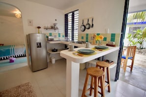 A compact kitchen with a refrigerator, a gas stove, and bar stools. - Nido Bacalar (Bacalar)