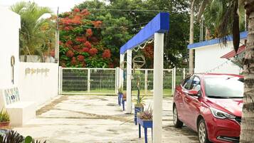 A gated parking area with a red car parked inside, surrounded by potted plants and a white fence.