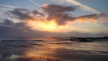 A beach with a sunset, clouds, and a visible contrail.