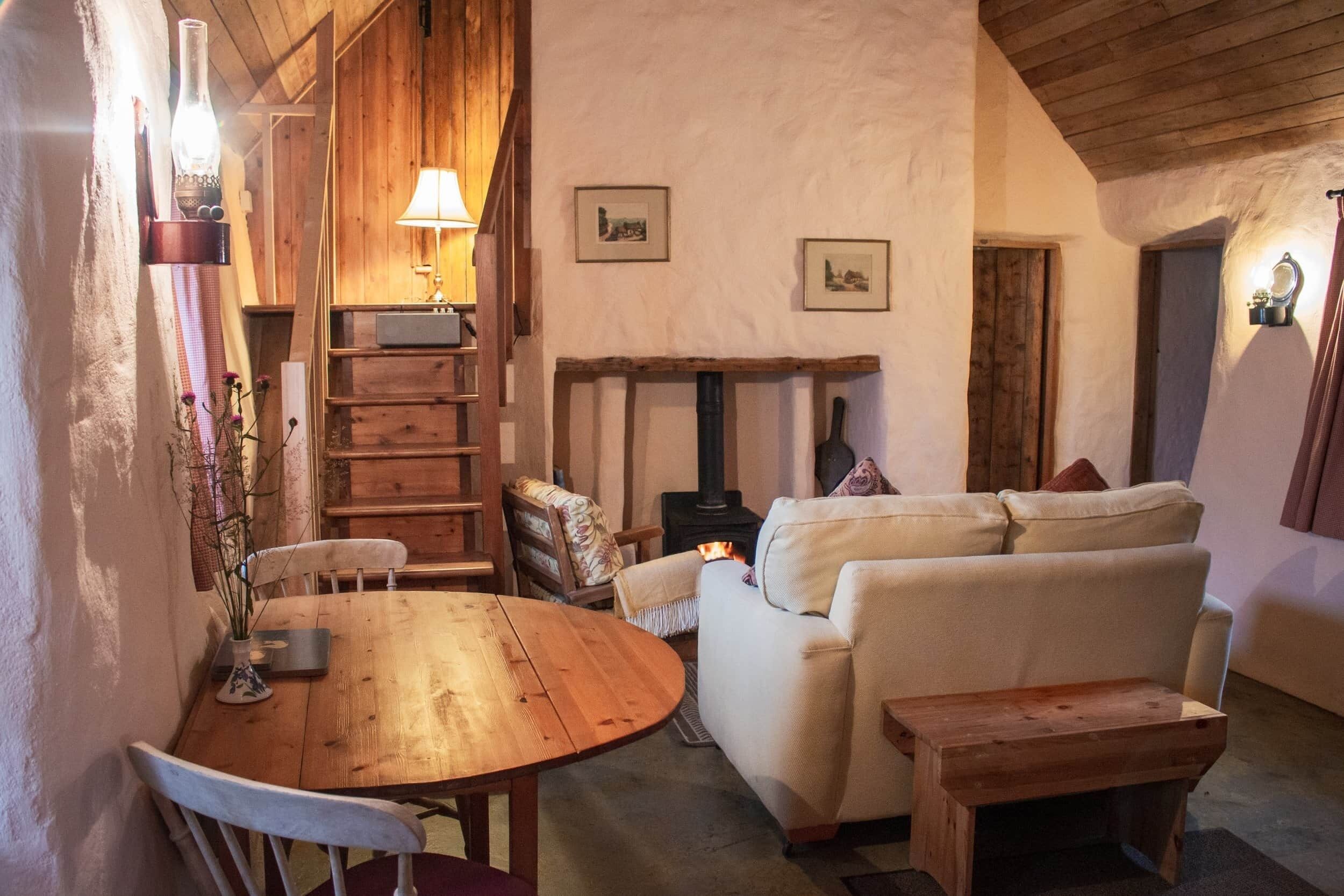 A cozy room with a wooden table, a sofa, a fireplace, and a lamp.