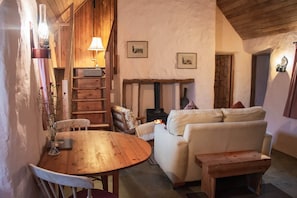 A cozy room with a wooden table, a sofa, a fireplace, and a lamp. - Historical Thatched Cottage @ Multi-Award-Winning Cnoc Suain (Galway)